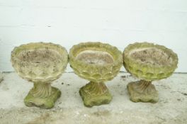 A set of three reconstituted stone urns on scroll feet,