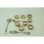 A collection of eight silver and silver coloured napkin rings; a silver serving spoon;