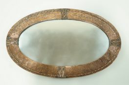 An Arts and Crafts style oval mirror with hammered and embossed copper frame, 75cm x 47.