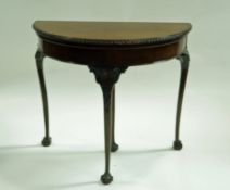 An early 20th century mahogany card table of demi lune form on carved cabriole legs on ball and