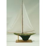 A pond yacht, the green painted hull with red stripe named Blowing Wind on stand.