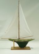 A pond yacht, the green painted hull with red stripe named Blowing Wind on stand.