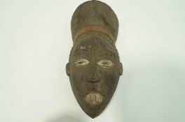 A carved Igbo face mask, painted black, with red and white highlights,