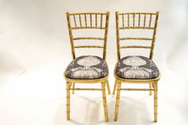 A pair of faux bamboo chairs, gold painted with padded seats.