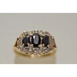 A sapphire and diamond 9 carat gold ring, the three oval cuts enclosed by eight single cuts,