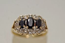 A sapphire and diamond 9 carat gold ring, the three oval cuts enclosed by eight single cuts,