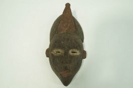 A carved Igbo face mask, painted black, with red and white highlights,