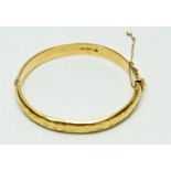 A 9ct gold hinged bangle, Birmingham 1965, of hollow D section and fully engraved, 0.9 cm wide, 6.