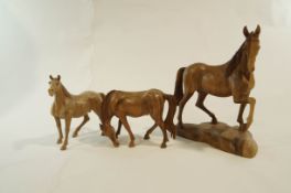 Three hand carved wooden models of horses in various poses,