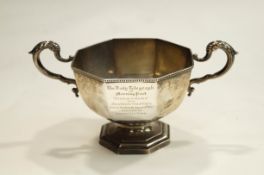 A silver octagonal trophy cup with two leaf-capped scroll handles and a golfing inscription,