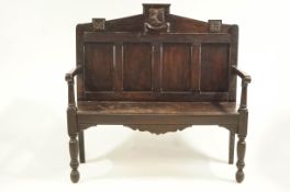 An 18th century and later oak hall bench, the panelled back with cresting rail,
