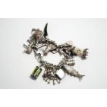 A silver bracelet, of solid curb links, with numerous charms attached,