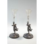 A pair of silver plated figures of boys dressed in finery, each holding a cut glass spill vase,