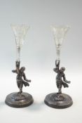 A pair of silver plated figures of boys dressed in finery, each holding a cut glass spill vase,