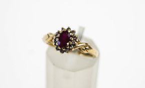 A 9 carat gold ruby and diamond cluster ring, the oval cut enclosed by twelve single cuts,