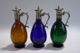 A set of three coloured glass claret jugs, each with silver plated mounts, 24.