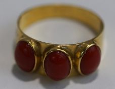 A three stone coral ring, stamped '750', the three uniform cabochons collet set, finger size P, 3.