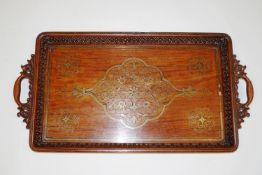 An Indian hardwood tray with decorative brass inlay and carved pierced handles,