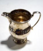A silver baluster cream or milk jug with a scroll handle, nulled rim on stepped foot,