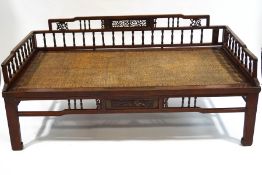 A Chinese hardwood and cane daybed, with turned spindle and fretwork panel sides,