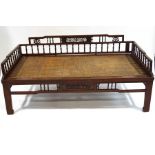 A Chinese hardwood and cane daybed, with turned spindle and fretwork panel sides,