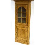 A pine standing corner cabinet, the upper section with arched glazed panel enclosing shelves,