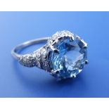 An aquamarine & diamond set dress ring in white metal, the claw set round cut aquamarine with