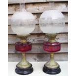 A pair of Victorian oil lamps with cranberry glass reservoirs