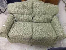 A modern two seat sofa with hump back and green self patterned scrolling upholstery