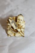 A Japanese carved ivory netsuke as a seated man with hobby horse,