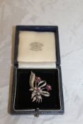 An 18 carat white gold ruby and diamond brooch set as a floral spray with leaf