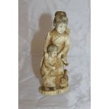 An early 20th Century Japanese carved ivory okimono as a woman with child feeding dog,