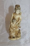 An early 20th Century Japanese carved ivory okimono as a woman with child feeding dog,