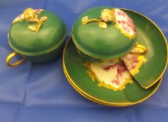 A pair of 19th Century Berlin porcelain chocolate cups and saucers with puce decoration on a green