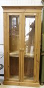 A modern pine two glazed door cupboard opening to reveal various shelving,