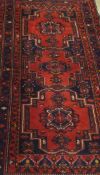 A Persian carpet with repeating medallions on a red ground within a blue and red banded floral