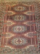 A Bokhara rug, the central panel set with four repeating elephant foot medallions on a rust ground,