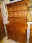 A pine dresser of two open shelves above two drawers and two cupboard doors,