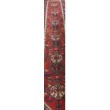 A Persian runner, the central red panel with repeating medallions in cream, dark blue,