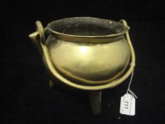 A 19th Century brass smelting pot with swing handle raised on three tapering supports