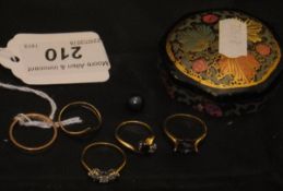 A small papier-mache type box containing a selection of gold and other dress rings,