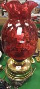 A large Victorian oil lamp with cranberry glass shade on a brass reservoir to pierced scrollwork
