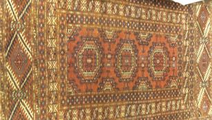 A Turkoman tribal rug, the three central medallions in terracotta, cream and blue/black,