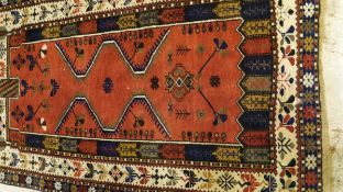 A Caucasian rug, the central terracotta field with geometric patterns in blue, gold,