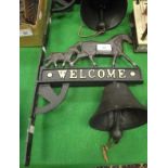 A cast iron bell mounted on a cast iron wall bracket decorated with horses and inscribed "Welcome",
