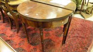 A Regency mahogany fold-over card table of demi lune form raised on turned and ringed tapering legs