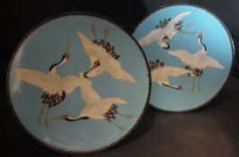 A pair of late 19th/early 20th Century cloisonné plates each decorated with three cranes on a sky