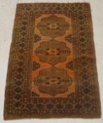 A Bokhara rug, the central panel set with three repeating medallions on a rust ground,