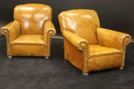 A pair of early 20th Century tan coloured leather and studded low arm chairs on bun front feet