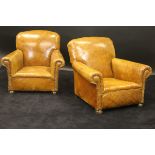 A pair of early 20th Century tan coloured leather and studded low arm chairs on bun front feet